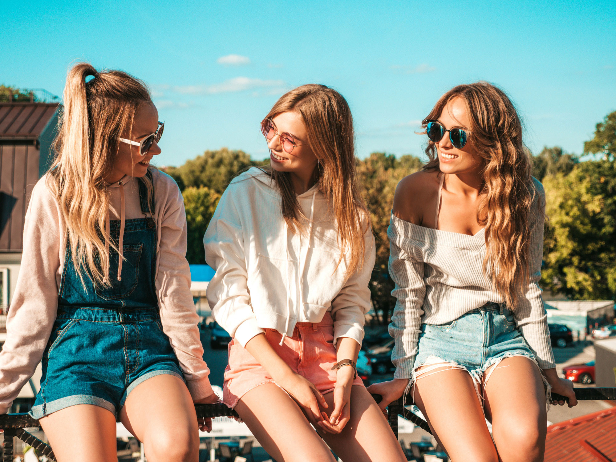 Three young women wearing sunglasses and casual summer clothes enjoying a sunny day outdoors together.