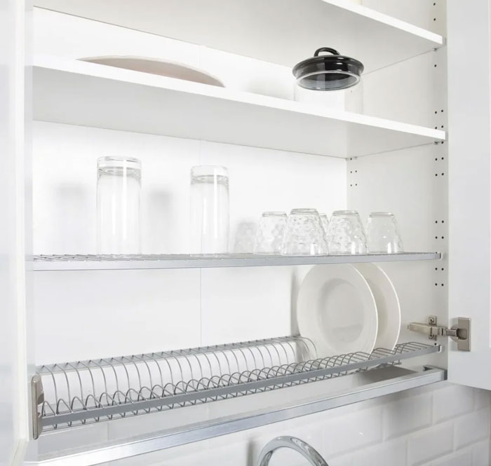 Glassware and plates neatly arranged in a dish drying rack inside a kitchen cabinet, a unique household item concept.