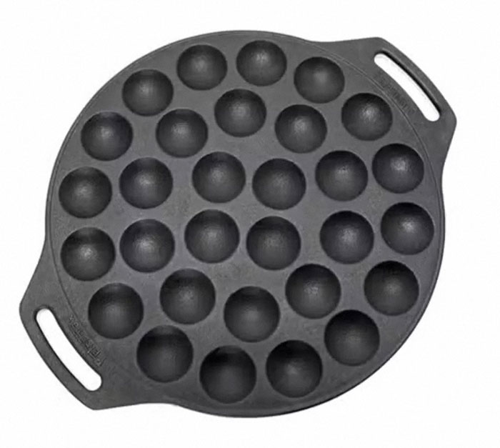 Cast iron pan with multiple round indentations used for cooking unique household items in specific countries.