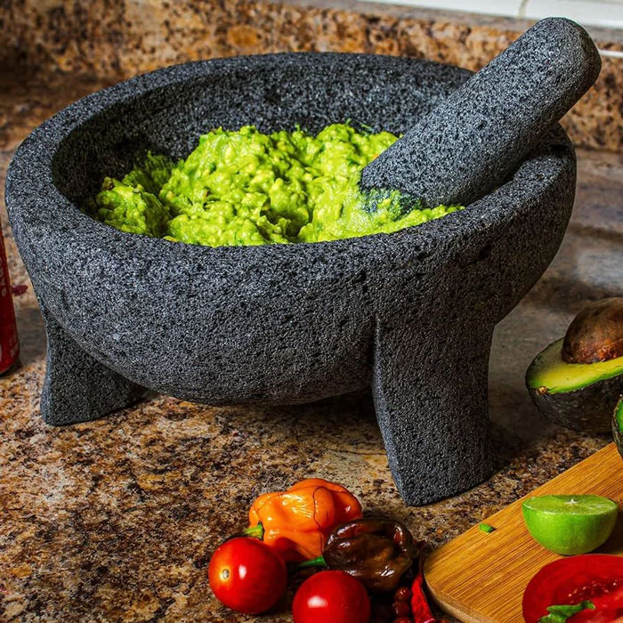 Traditional Mexican mortar and pestle made of volcanic stone with freshly mashed avocado inside.