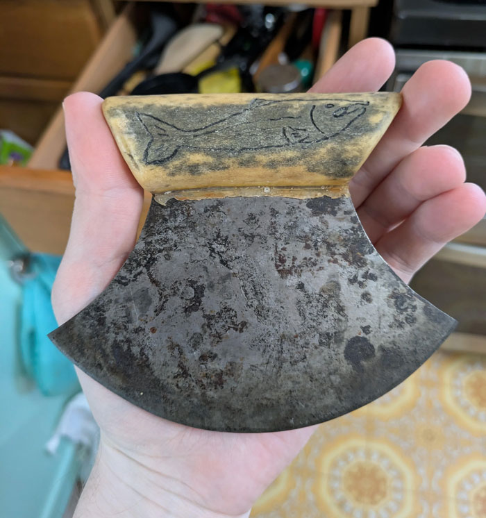 Hand holding a unique household item with a carved fish handle, showcasing rare cultural kitchen tools.