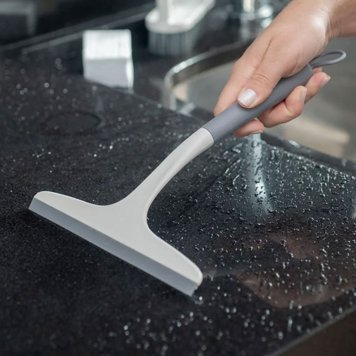 Hand using a squeegee on a wet black countertop, a unique household item shared from different countries.