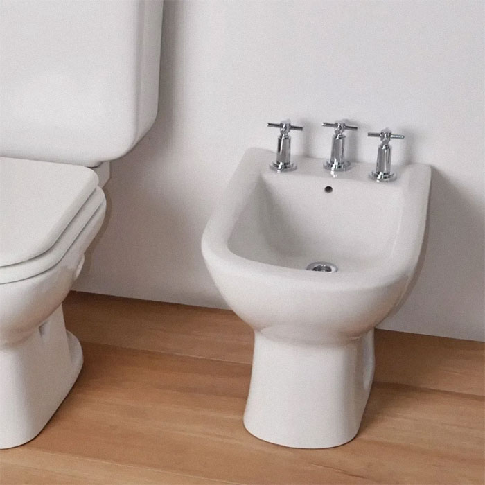 White bidet with three chrome taps next to a toilet, a unique household item found in some countries only.