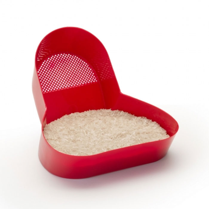 Red plastic household item used for rinsing rice in unique countries, showing grains inside the container.