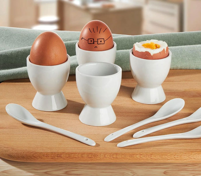 White ceramic egg cups and spoons on a wooden board, a unique household item shared by 100 people worldwide.
