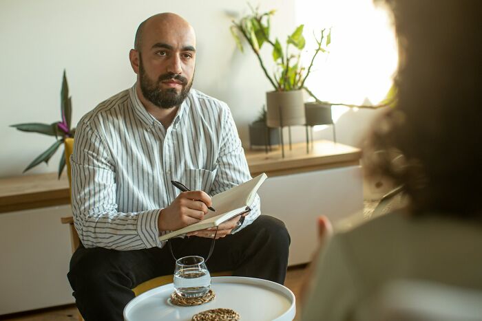 Man taking notes while listening to a patient in a calm room, illustrating unethical doctor and patient interaction.