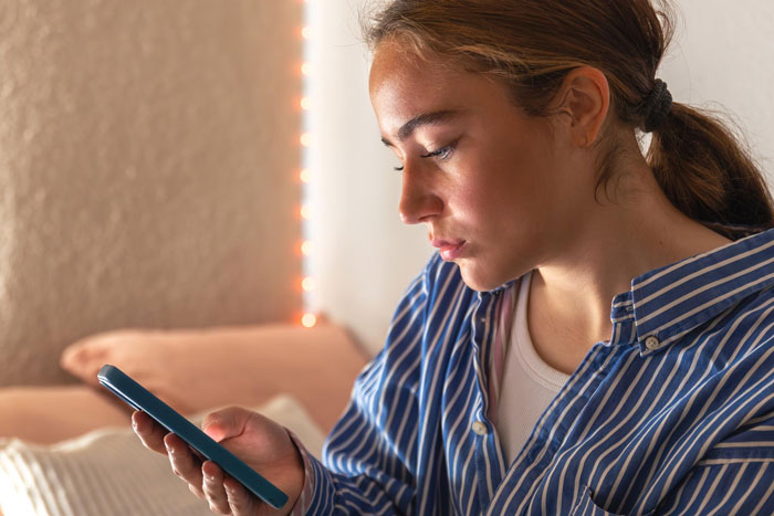 Young pregnant woman looking worried while holding a phone, concerned about co-parenting with bipolar guy and young lover.