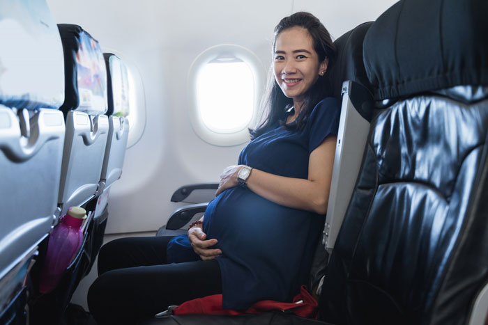 Pregnant woman smiling on an airplane seat, concerned about co-parenting with her bipolar husband after their breakup.