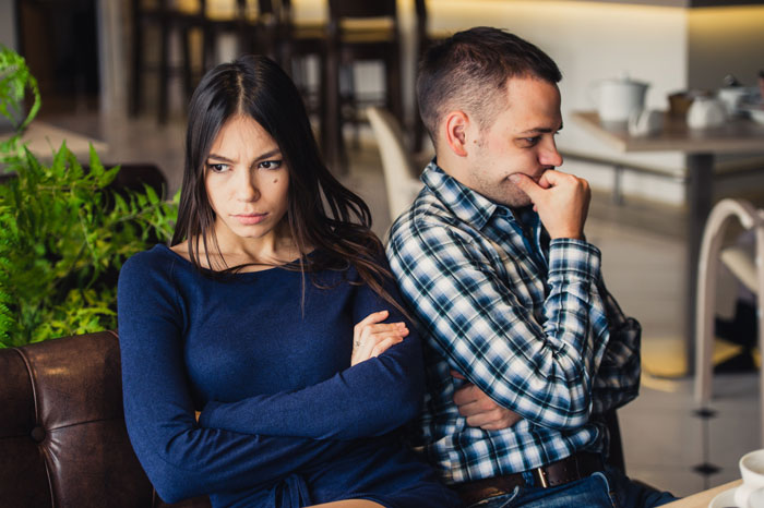 Woman and man sitting back to back in a caf&eacute;, tense and upset over a casual boyfriend&rsquo;s hidden piece on the side situation.