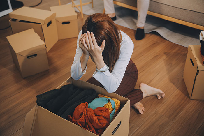 Woman sitting on floor overwhelmed by packing boxes, refusing to move after decades relocating for husband’s career. Woman sitting on floor overwhelmed by packing boxes, refusing to move after decades relocating for husband’s career.