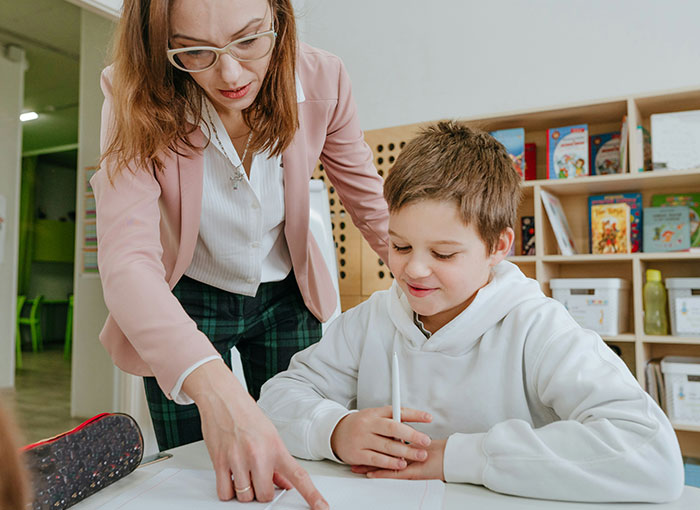 Teacher helping a smiling boy with a fun fact in a classroom, highlighting a moment of learning and discovery. Teacher helping a smiling boy with a fun fact in a classroom, highlighting a moment of learning and discovery.