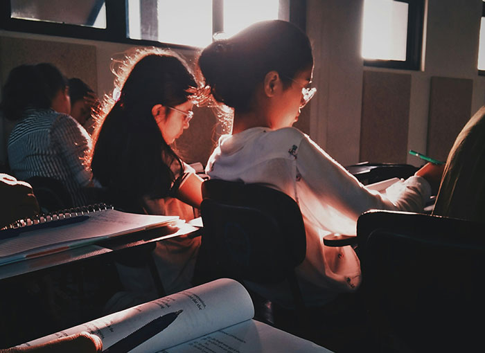 Student in classroom confidently sharing a fun fact with teacher while others focus on their work. Student in classroom confidently sharing a fun fact with teacher while others focus on their work.