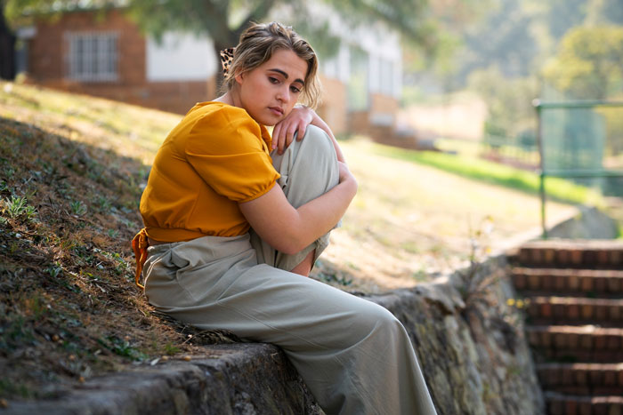 Young woman sitting alone outdoors, looking thoughtful and upset, depicting challenges of toxic guy and wife's autonomy issues.