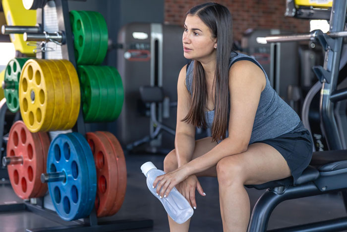 Woman showing independence and autonomy while resting in gym, holding a water bottle and looking thoughtful.