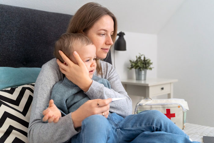 Wife holding sick child on bed, looking tired and frustrated, reflecting feelings of being fed up and overwhelmed when caring for family. Wife holding sick child on bed, looking tired and frustrated, reflecting feelings of being fed up and overwhelmed when caring for family.
