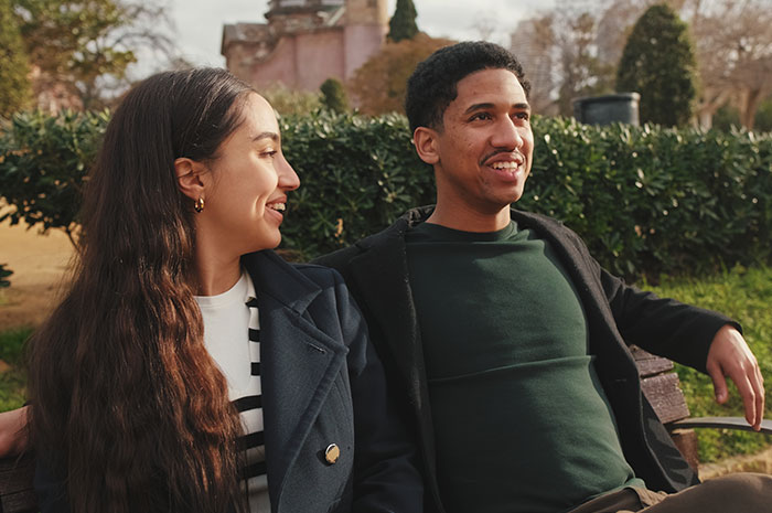 Couple sitting outdoors smiling and enjoying a moment together before husband parents coming honeymoon surprise.