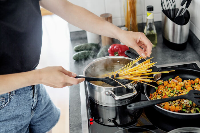 Mom with hygiene anxiety preparing pasta in kitchen, focusing on cleanliness and careful cooking process.