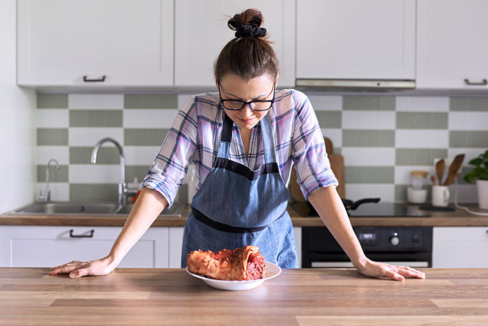 Woman in apron looking upset at a messy piece of food on plate, depicting a wife furious after husband embarrassment.