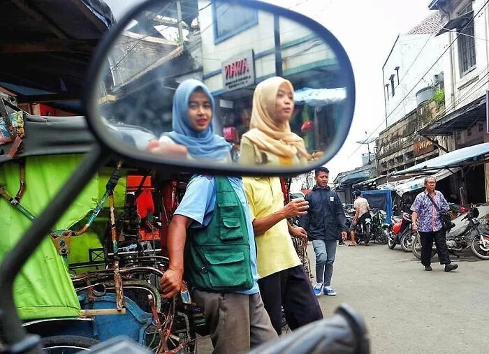 Two women wearing hijabs reflected in a motorcycle mirror in a busy urban street shot perfectly timed by a photographer.