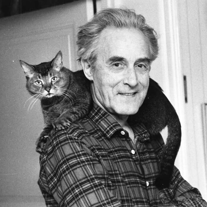 Vintage black and white photo of a man smiling with a cat on his shoulder showcasing timeless feline charm.