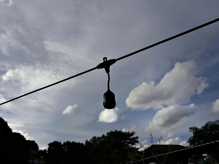Silhouette of a hanging street light against a cloudy sky, showcasing a perfectly timed street shot by the photographer.