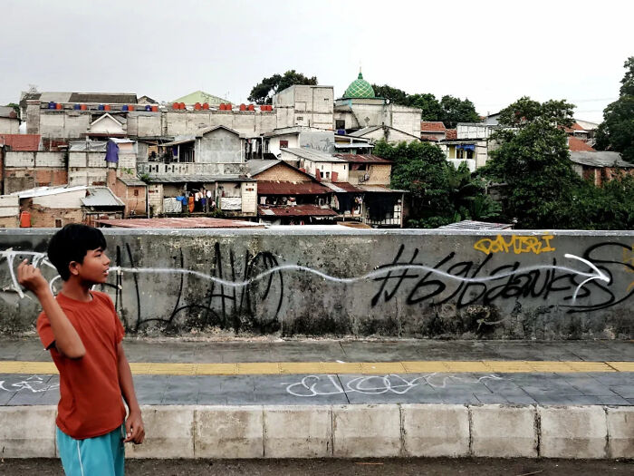 Boy in an orange shirt captured in a perfectly timed street shot with urban buildings and graffiti in the background.