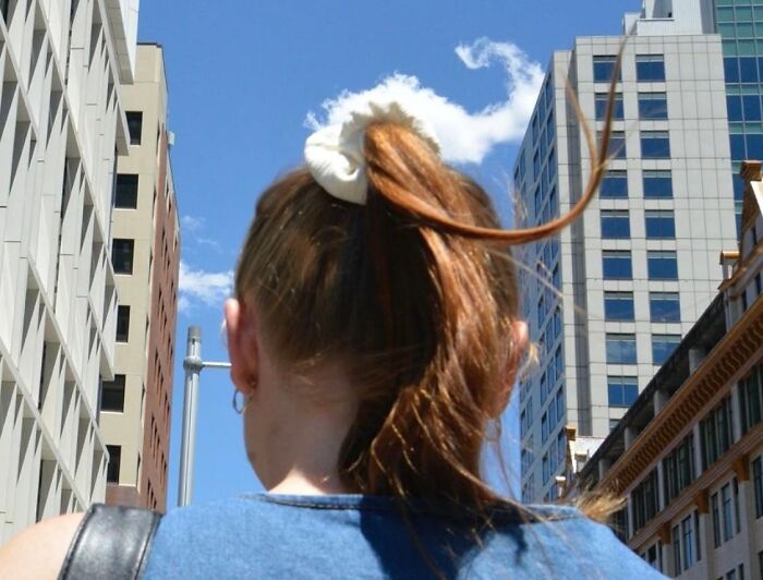 Street photographer captures perfect coincidences of a woman’s ponytail flowing against an urban cityscape background.