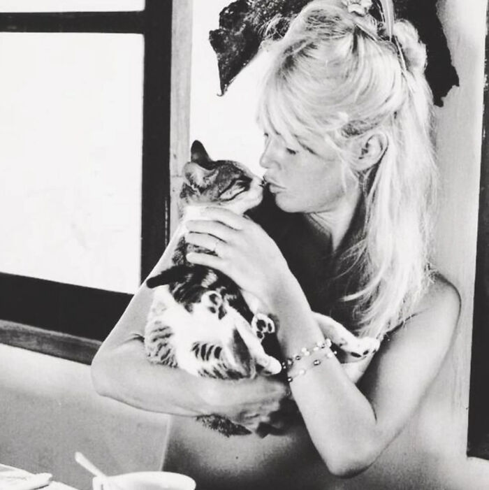 Woman holding and kissing a cat in a vintage black and white photo capturing timeless feline charm and affection.