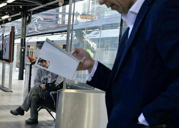 Street photographer capturing a perfect coincidence of a man reading with a seated passenger at a train station.