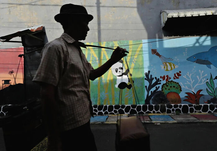 Silhouette of a man walking past colorful street art featuring a panda and ocean creatures in a perfectly timed street shot.