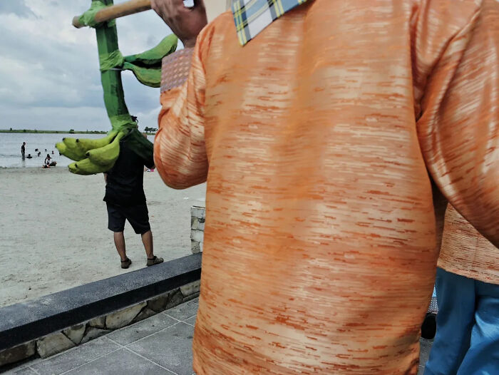 Street photography capturing a perfectly timed moment with people and large green bananas near a waterfront scene.
