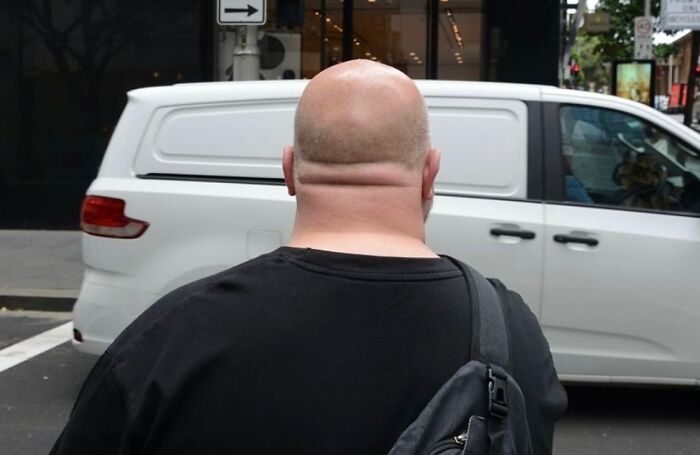 Street photography capturing a bald man perfectly aligned with a white van creating a visual coincidence on a city street.