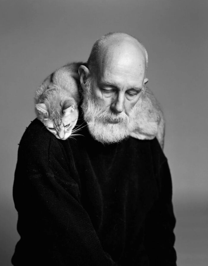 Older man with a vintage cat resting on his shoulder, showcasing timeless feline charm in a black and white photo.