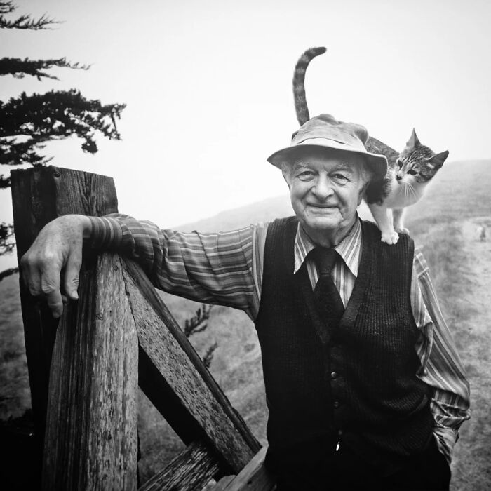 Vintage black and white photo of a smiling elderly man with a cat on his shoulder showcasing timeless feline charm.