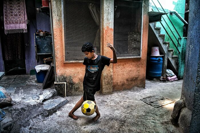 A candid street photo of a barefoot boy playing soccer in a rustic urban setting capturing humanity and everyday life.
