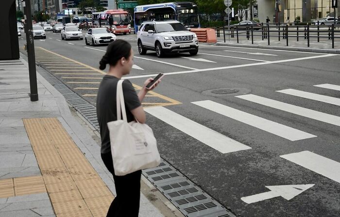 Woman standing near crosswalk on busy street, capturing a perfect coincidence moment in street photography.