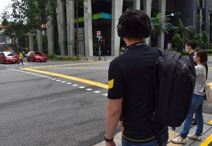 Street photographer wearing headphones and backpack, standing at a crosswalk, capturing perfect coincidences in the urban scene.