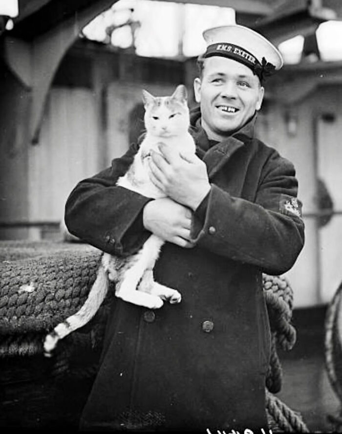 Vintage black and white photo of a sailor holding a cat, showcasing timeless feline charm from history.
