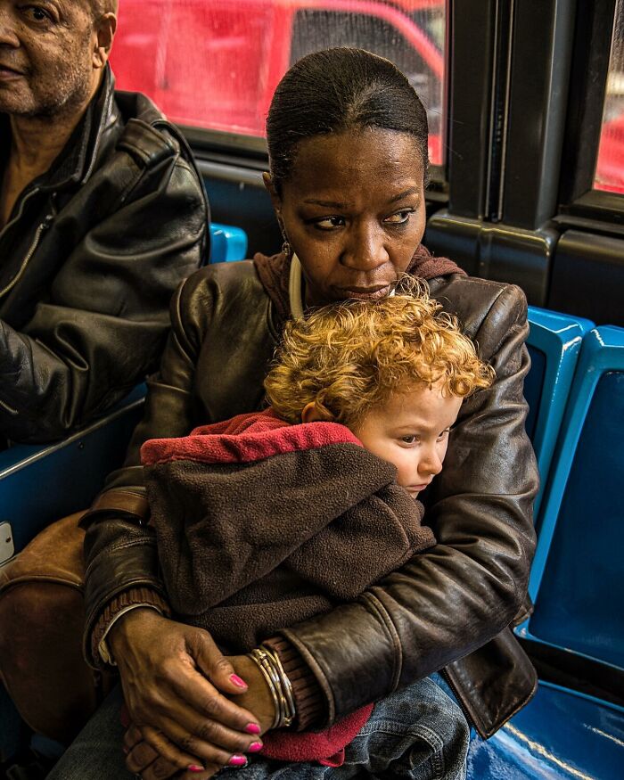 Woman holding child on public transport, capturing tender moments in candid street photos showing humanity and emotion.