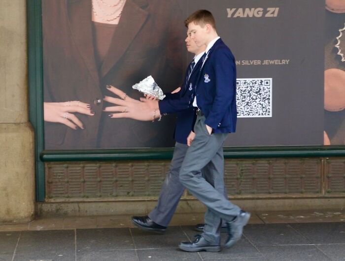 Two young men walking past an advertisement, captured by street photographer focusing on perfect coincidences.