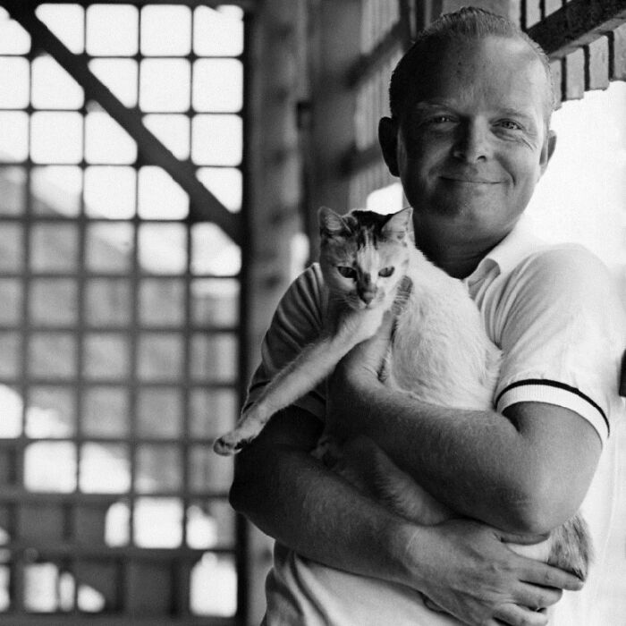 Smiling man in a vintage black and white photo holding a cat, showcasing timeless feline charm and affectionate bond.