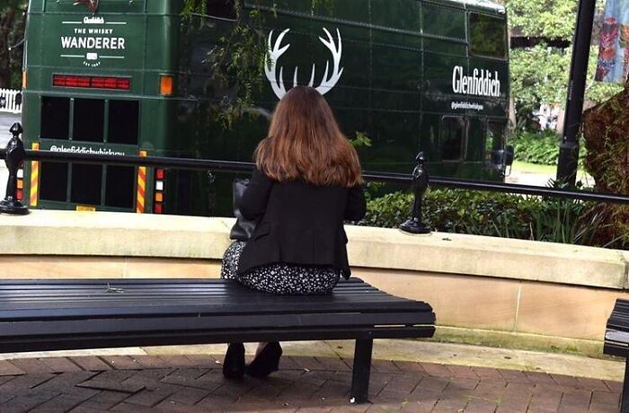 Woman sitting on a bench perfectly aligned with antlers on a passing vehicle, capturing a perfect street photographer coincidence.
