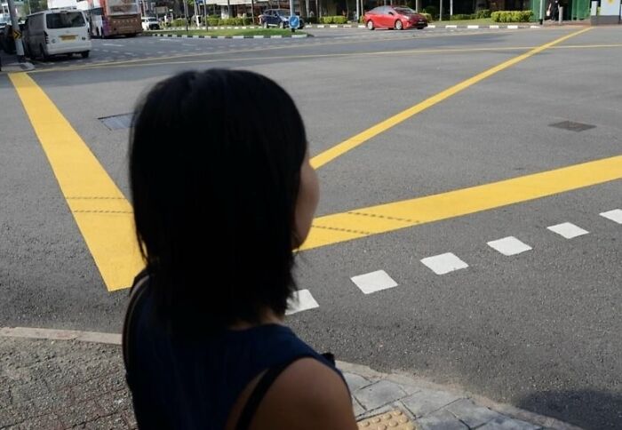 Woman at a street corner aligned with bold yellow road lines, showcasing perfect street photography capturing coincidences.
