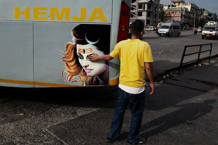 Boy in a yellow shirt touching a painted face on a bus in a candid street photo capturing humanity and absurdity.