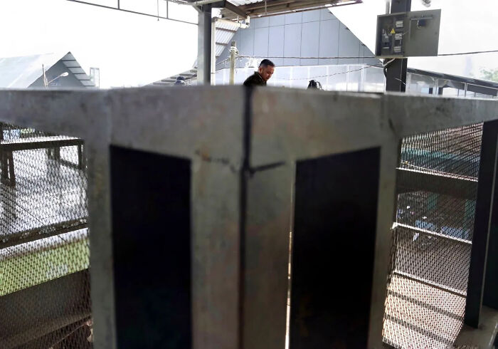 Street shot capturing a man walking behind a metal structure in an industrial urban setting with dramatic lighting.
