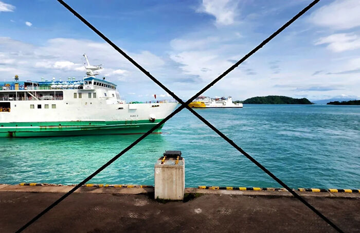 A perfectly timed street shot of ships docked at a pier with clear blue water and a bright sky in the background.