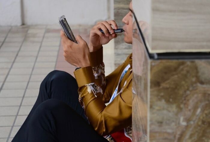 Man sitting on tiled floor playing a harmonica, capturing perfect coincidences in street photography at the right moment.