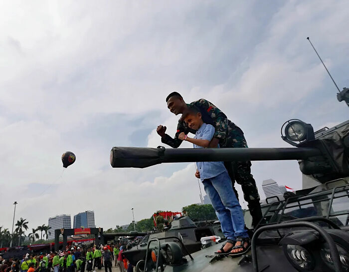 Child and soldier on military vehicle, captured in a perfectly timed street shot during a public event.