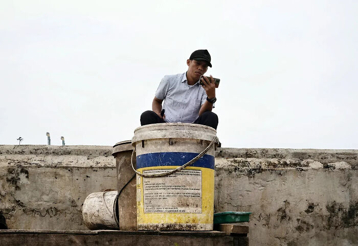 Man sitting on large bucket while looking at phone in a street shot captured with perfect timing by a photographer