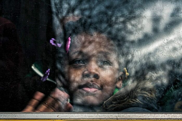 Candid street photo of a young girl looking through a window, capturing a tender moment and humanity.